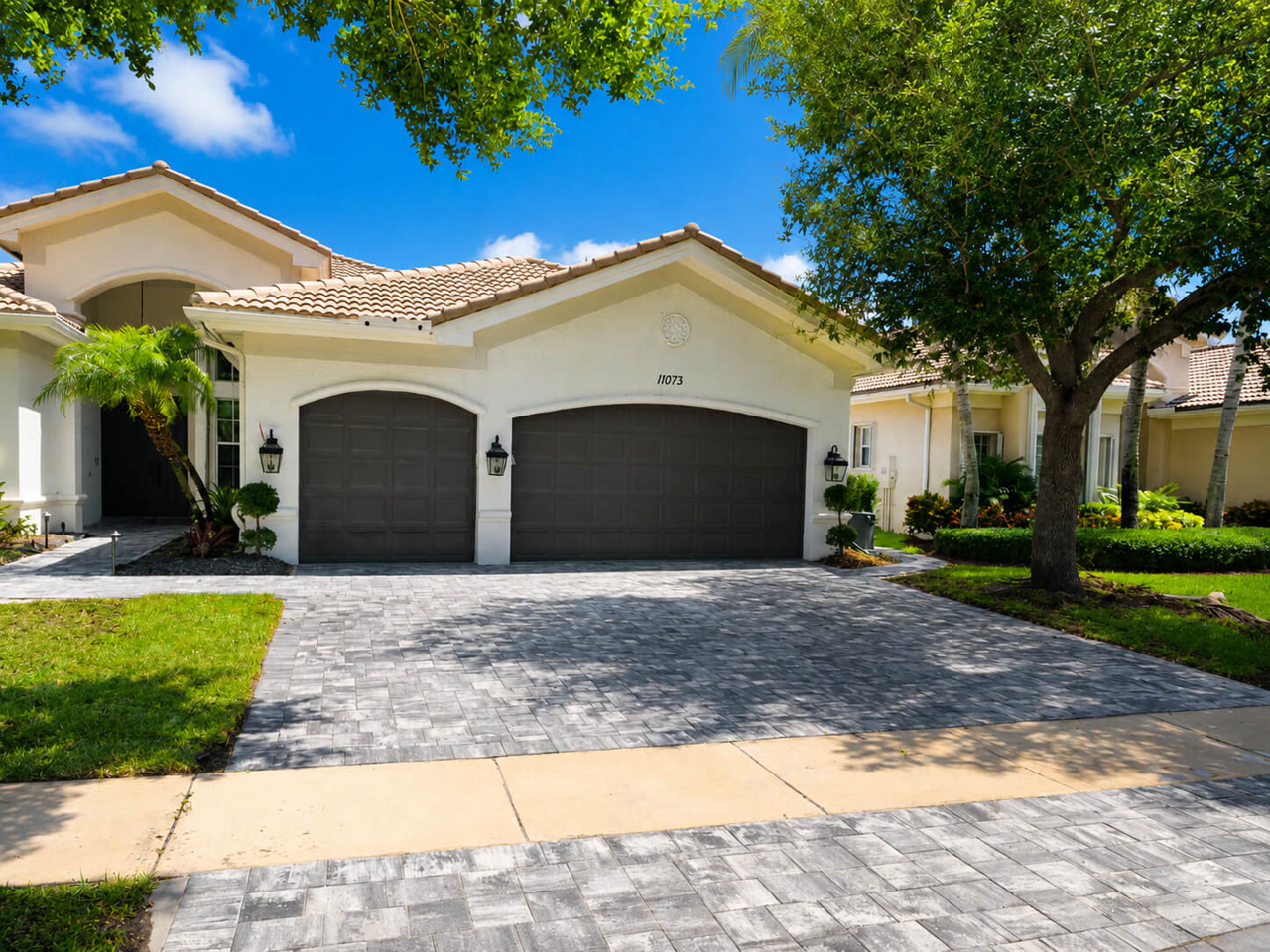 Finished gray paver driveway spanning a three car garage at a Mediterranean style home on a Greenacres property