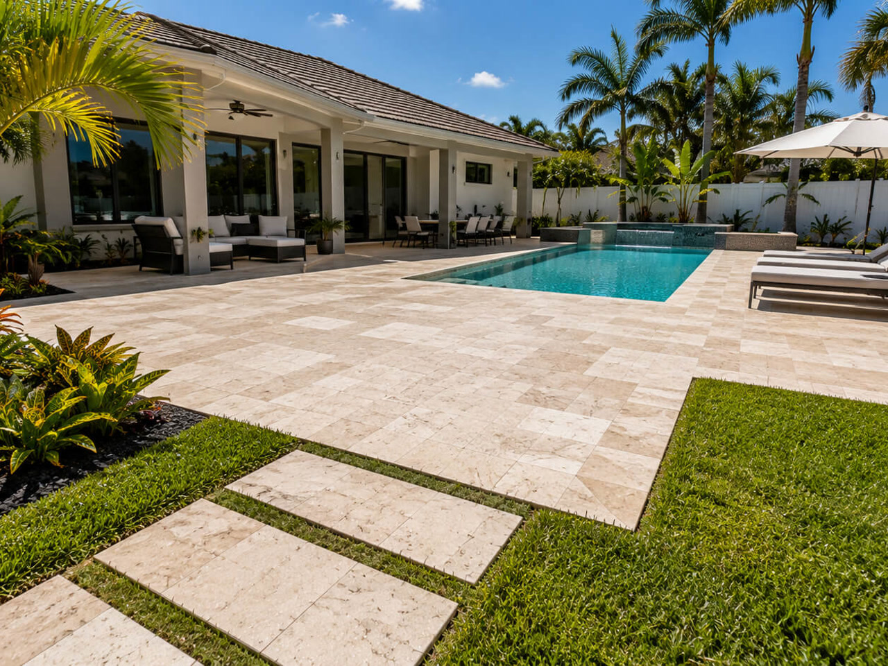 Travertine paver patio beside a pool with a stepping stone walkway leading to the lawn on a Juno Beach property