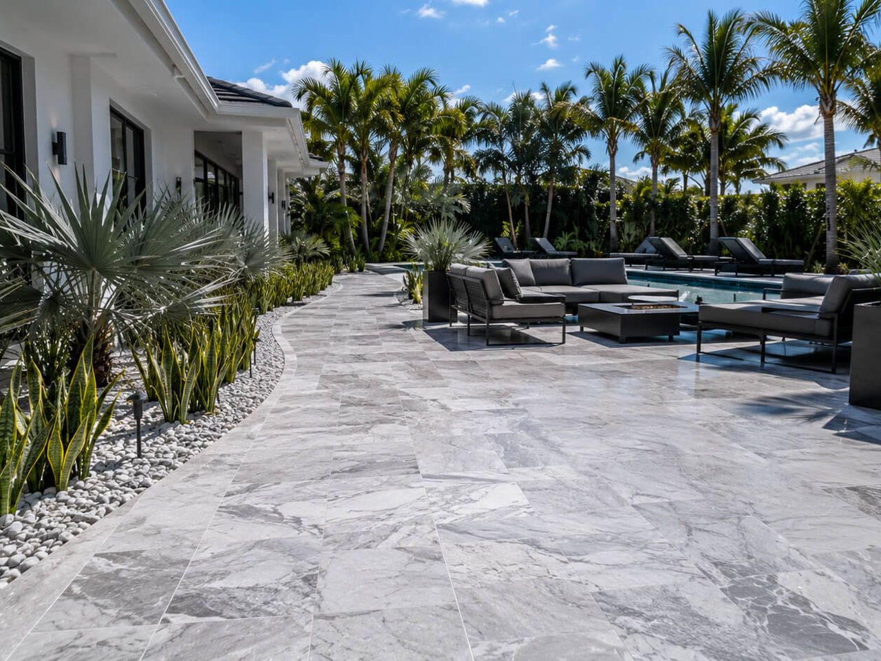 Gray marble paver patio curving along a modern home to a poolside lounge with a fire table at a Palm Beach Gardens residence