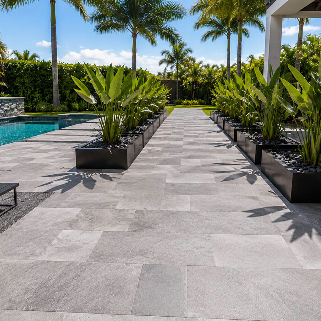 Gray paver walkway between black planters connects the pool deck to the backyard on a Pompano Beach property