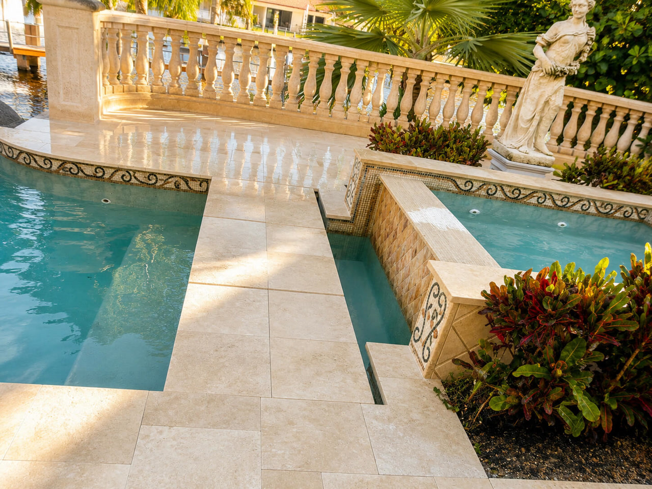 Ivory paver pool deck with a stone balustrade and mosaic tile spillway at a waterfront estate in Gulfstream