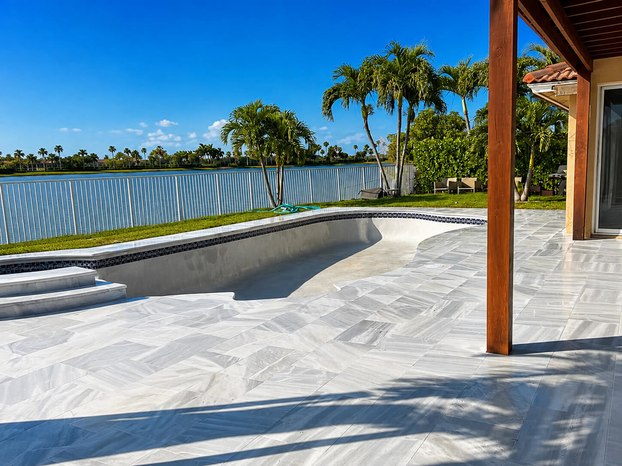 Drained pool shell with fresh gray surface prepared for resurfacing, ringed by a new marble paver deck for a Boynton Beach homeowner