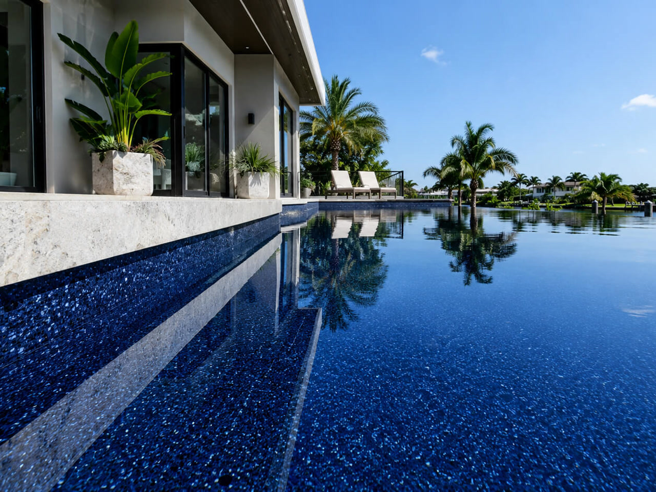 Finished pool resurfacing in a dark pebble finish, with sheer descents spilling over gray marble coping at a Hypoluxo pool