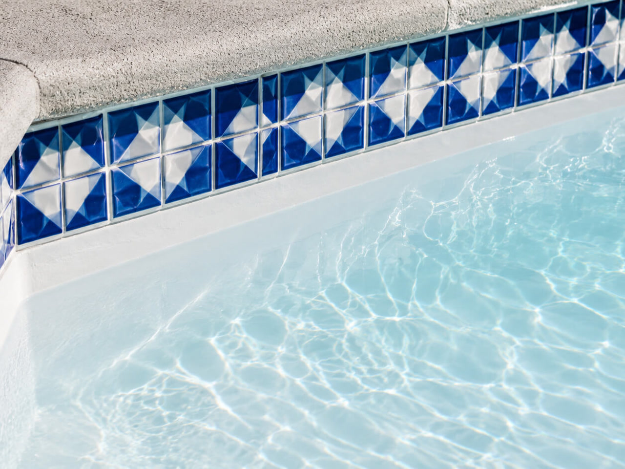 Classic white plaster pool finish under a blue and white patterned tile border and textured concrete coping, on a Loxahatchee property
