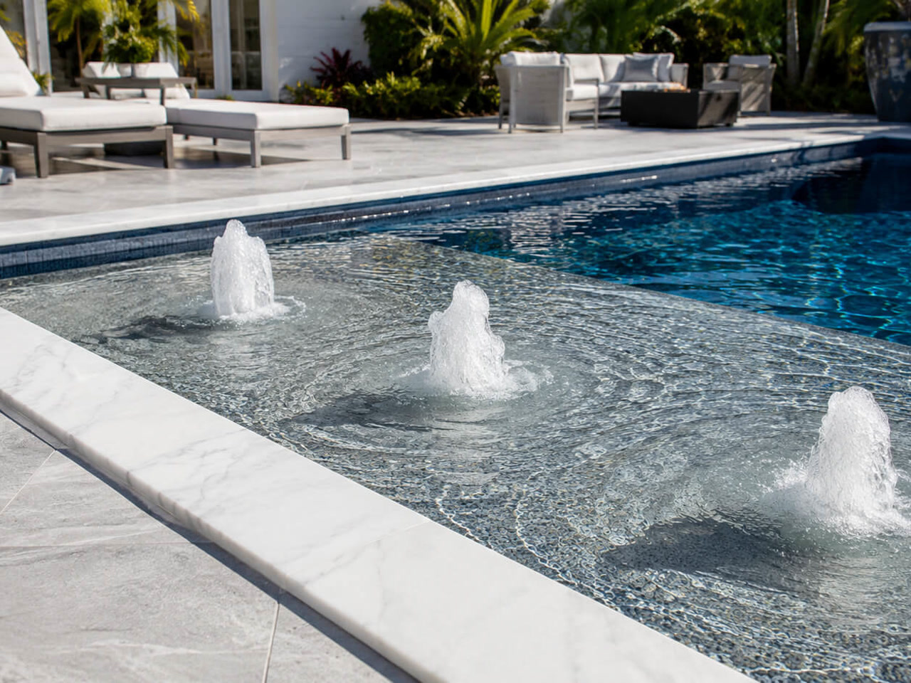 Three bubblers running across a mosaic tiled sun shelf edged in white marble coping for a Juno Beach homeowner