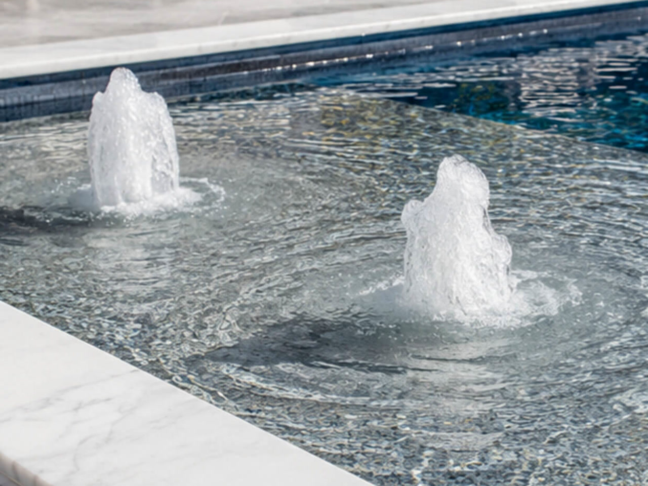 Two bubbler fountains on a mosaic tiled sun shelf edged with white marble coping in Jupiter