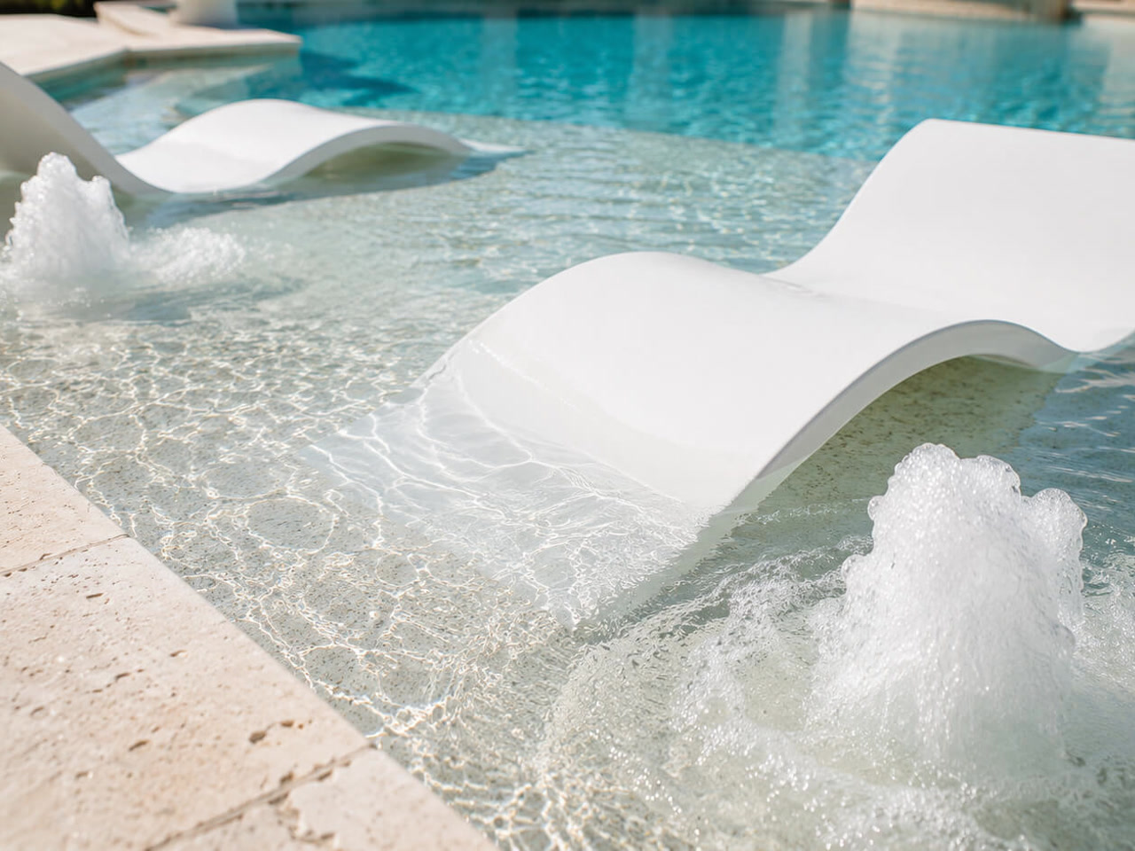 White in water loungers on a shallow sun shelf with bubblers churning on either side at a Jupiter home