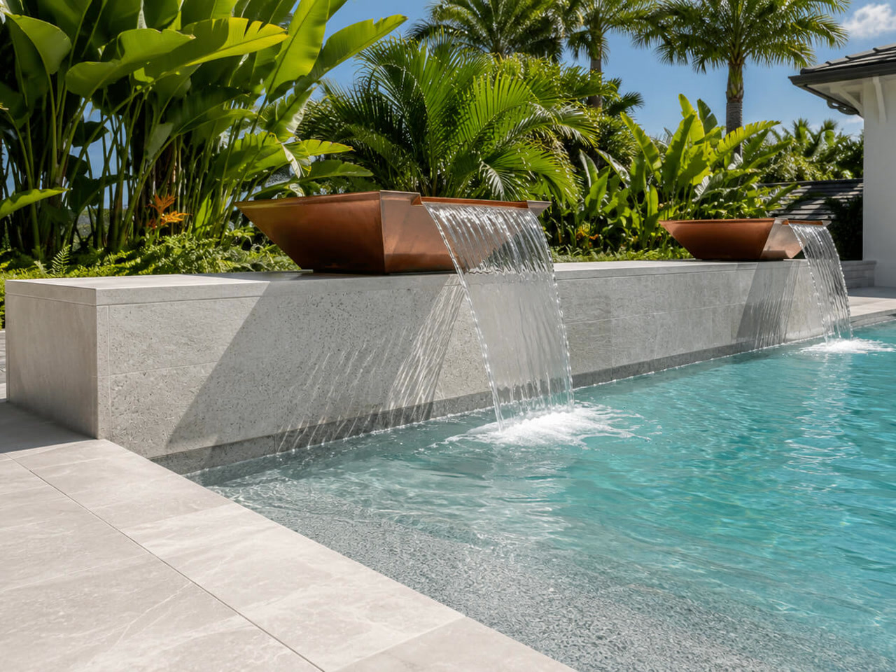 Copper scupper bowls spilling over a light stone wall into a pool framed by tropical planting in Jupiter