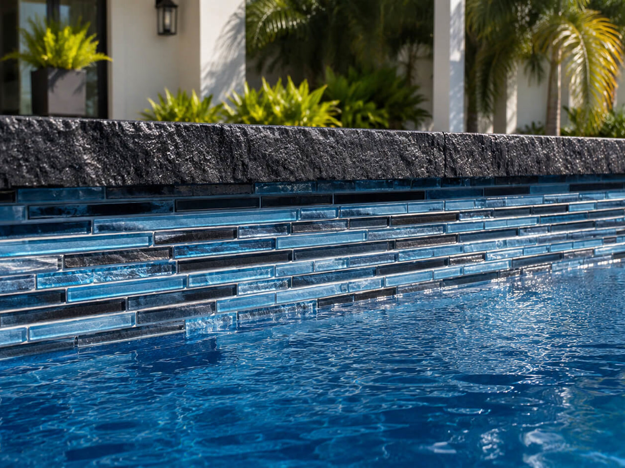 Rough cut black stone coping over linear blue glass waterline tile at a finished West Palm Beach pool edge