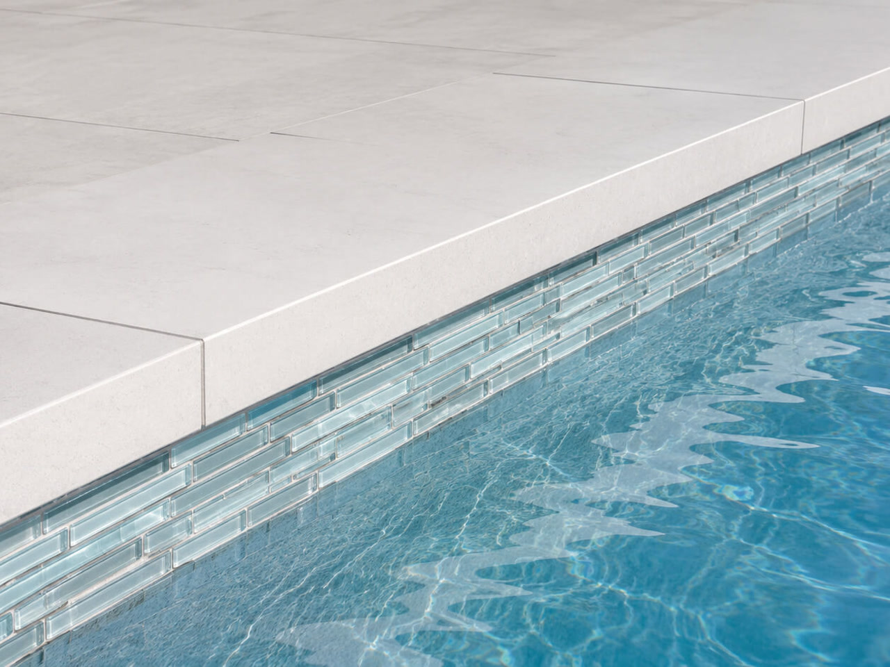 Squared off light stone coping over a linear pale blue glass waterline tile band at a West Palm Beach pool