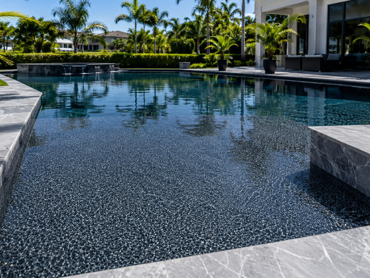 Renovated pool with a dark charcoal pebble interior finish and gray marble coping and steps