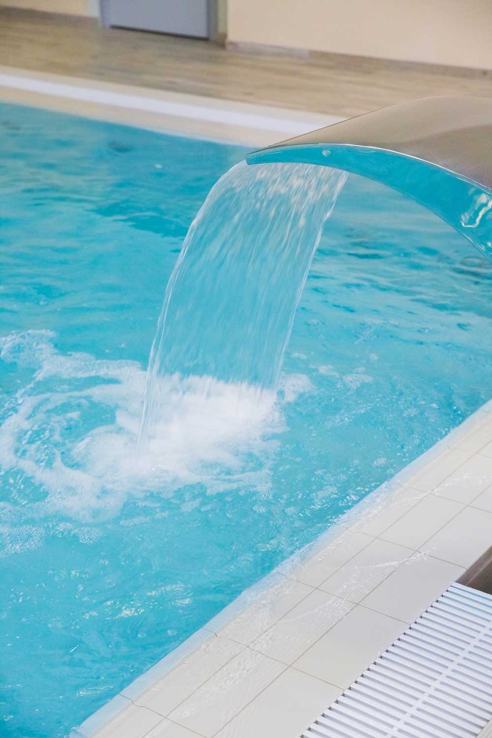 Curved stainless steel waterfall pouring into a swimming pool